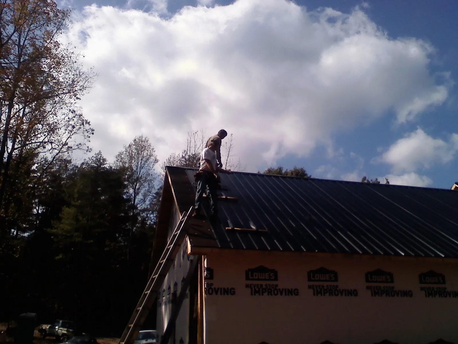 Roofer fastening dark metal panels high against a cloudy sky, from a Roof Inspection job in Cartersville