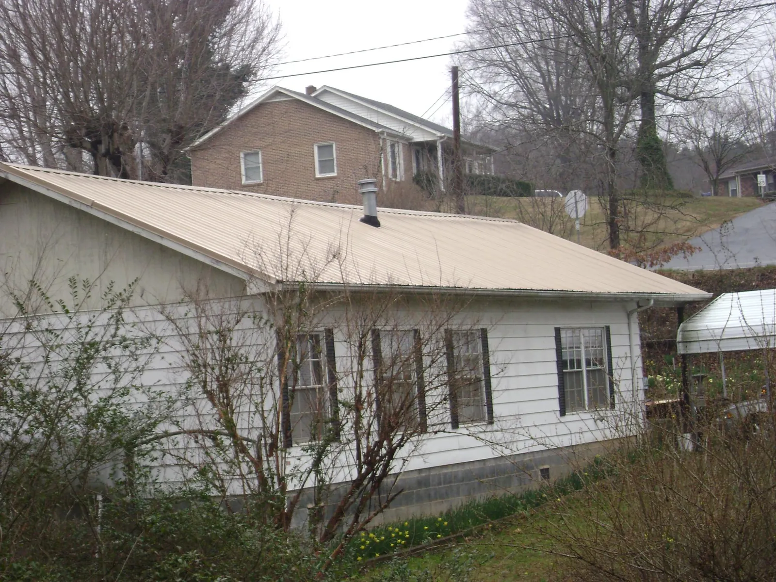 Tan metal roof on a white sided house set into a hillside — Commercial Roofing by Roofing Brothers in Cartersville